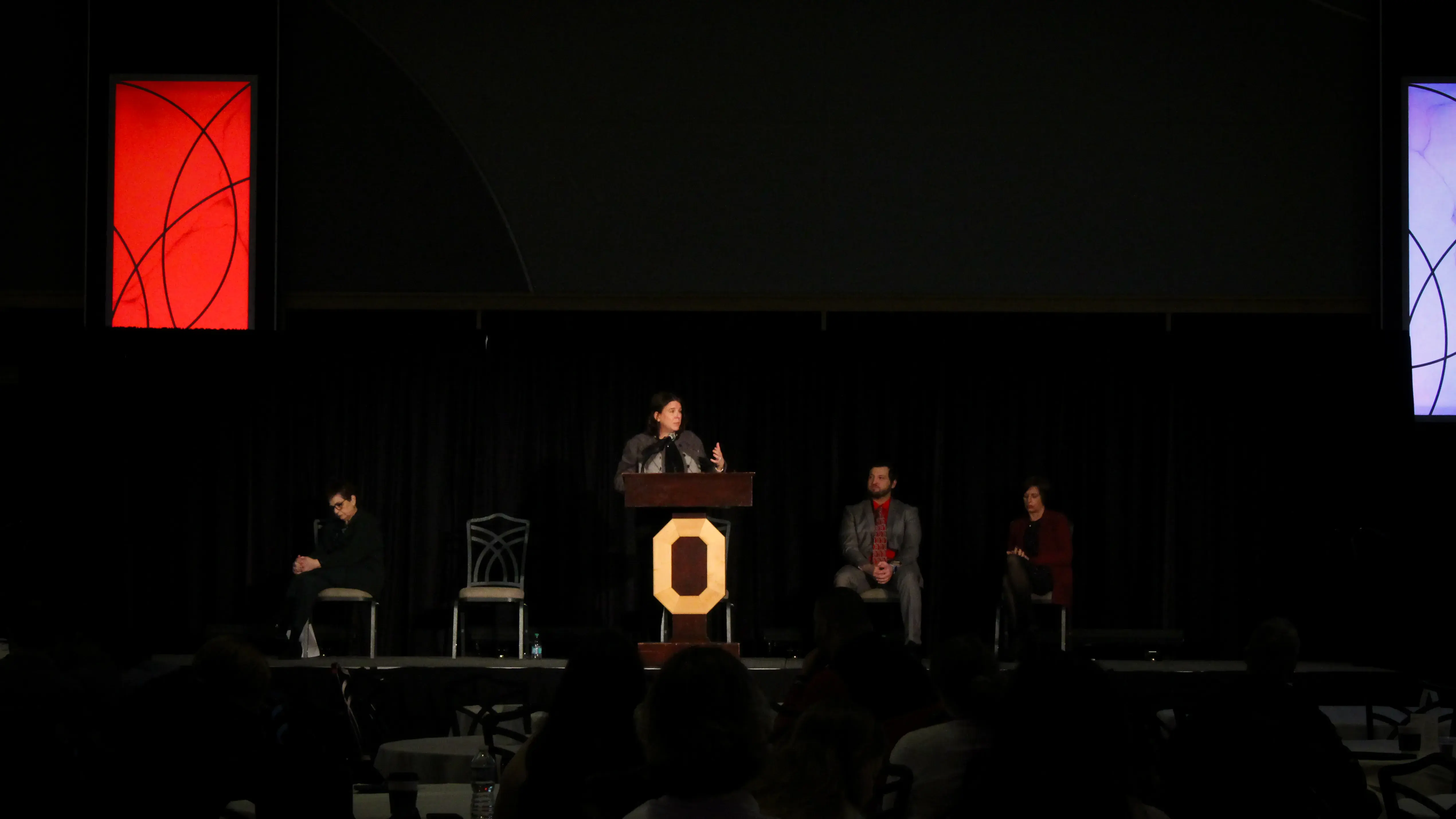 Lori Criss speaking at a podium, with multiple other doctors on the background