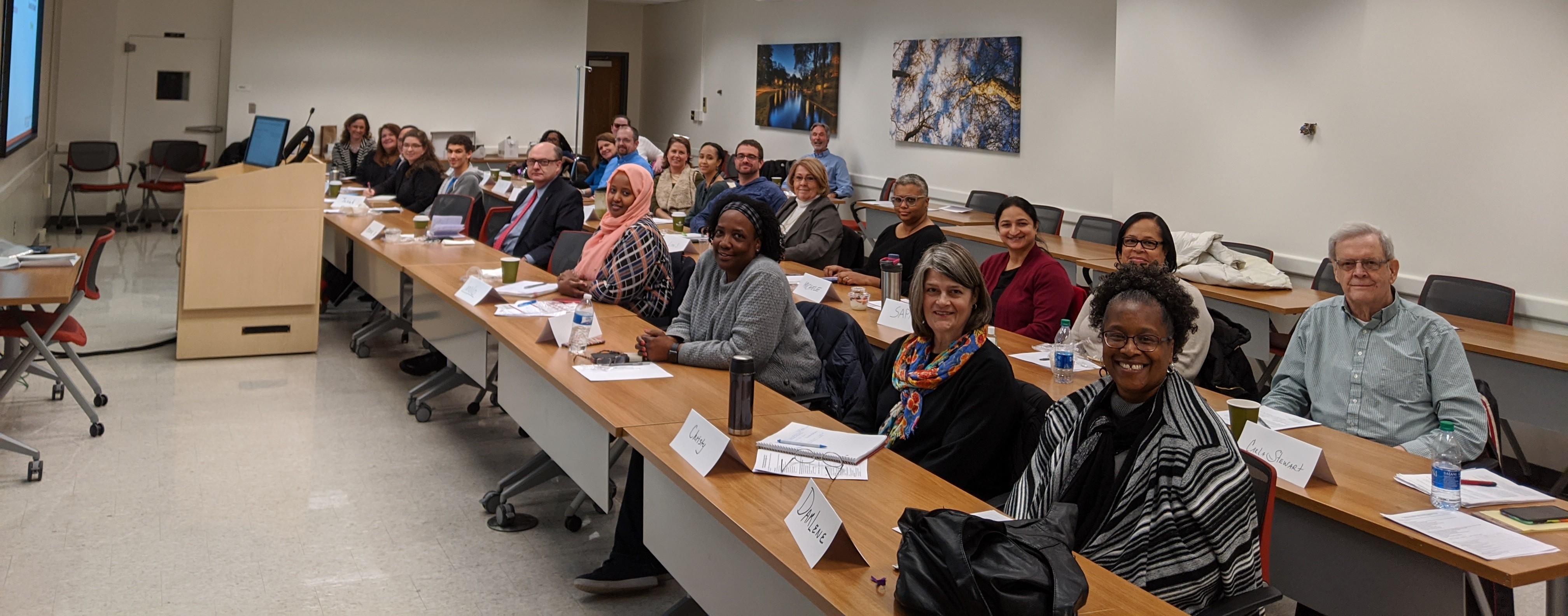 large group of people in a classroom setting sitting at long rows of desks smiling for the camera