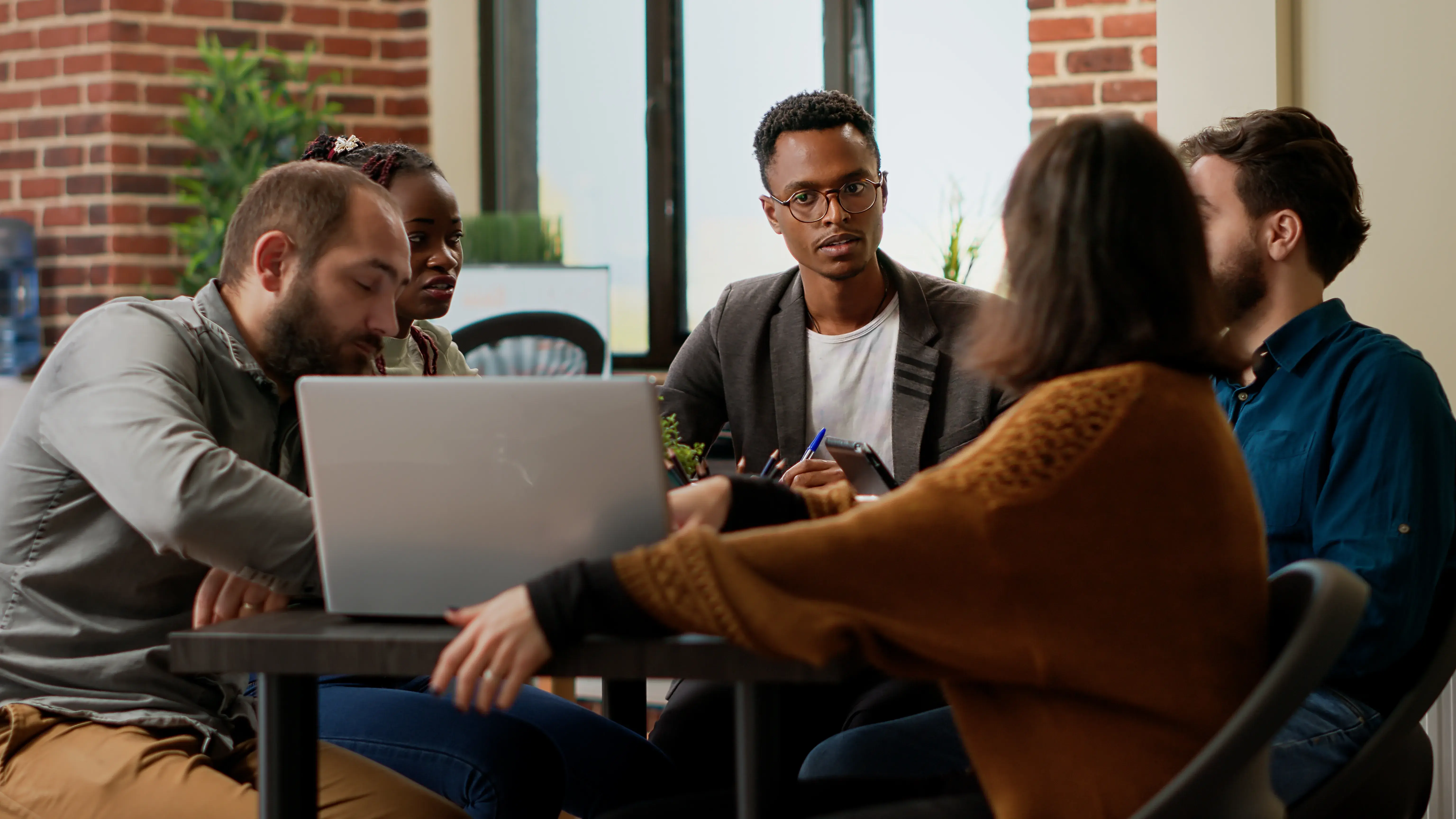 Group of men and women sitting at a table, conversing over a laptop