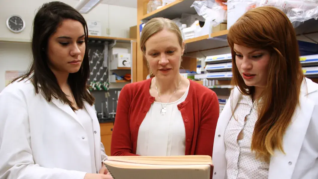 three women in a laboratory setting looking over a list of documents