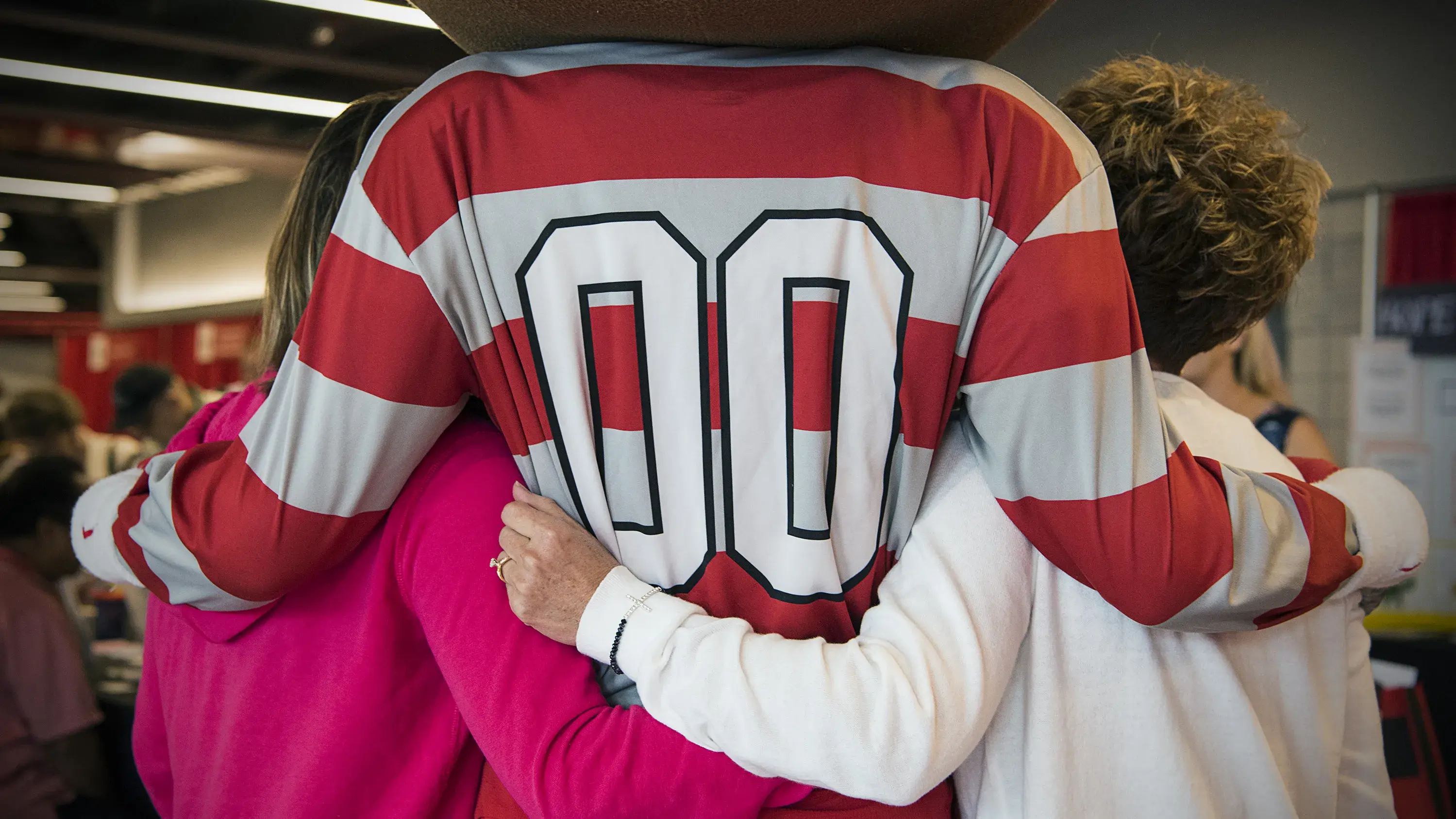 Back of Brutus Buckeye with his arms around two children and their arms around him.