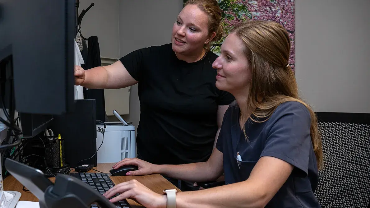 Two women using an online system in front of a computer screen and keyboard