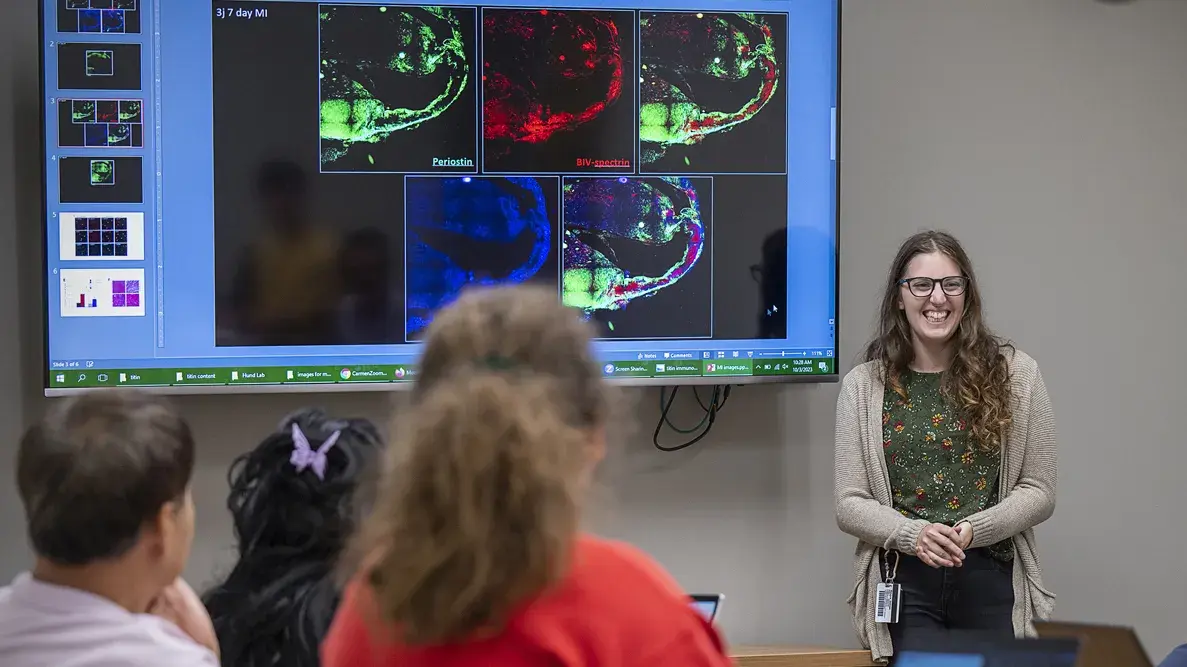 A female researcher presenting her research on a tv monitor to a group of indivduals 