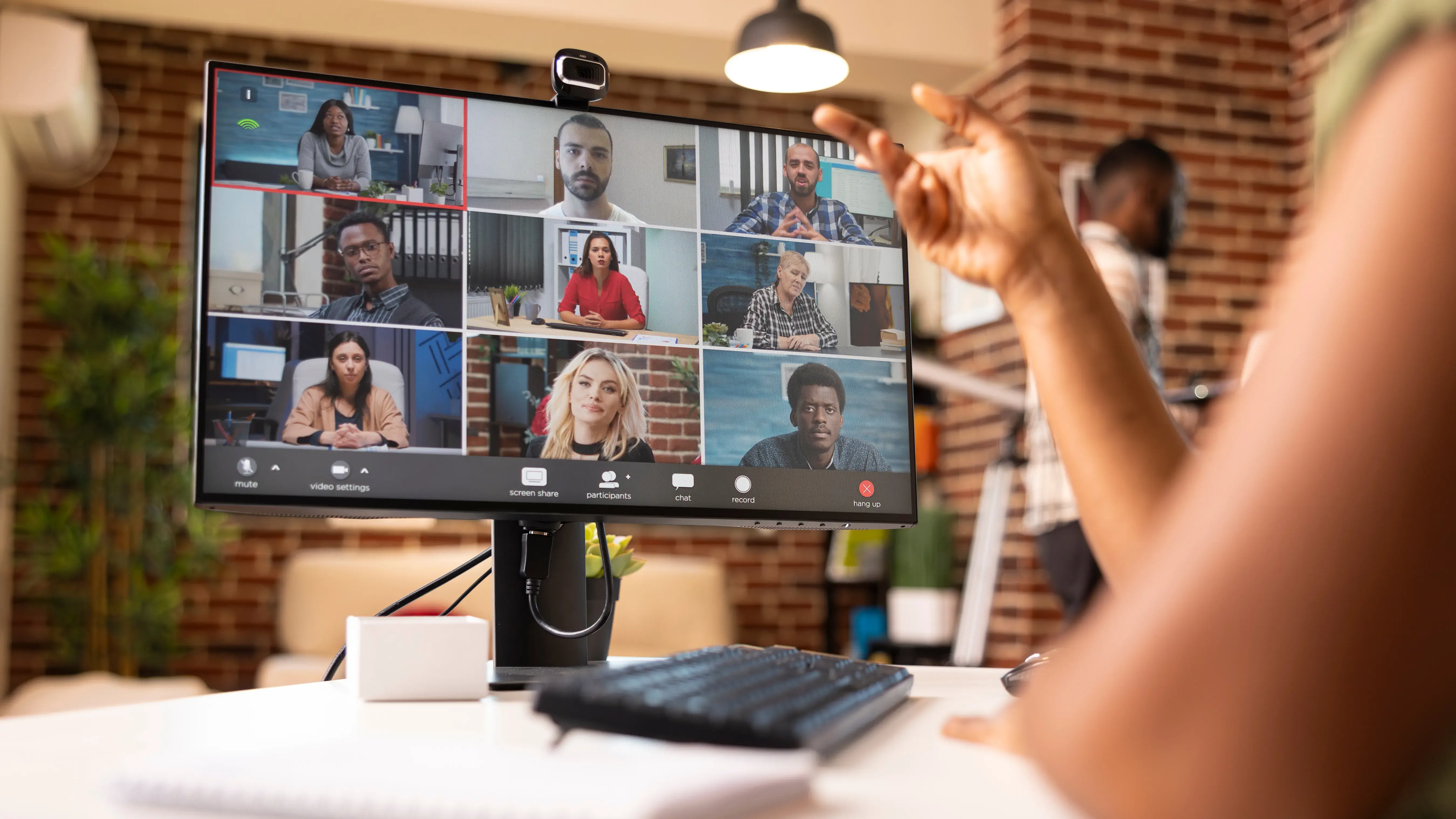 Professional individual in apartment, leading brainstorming session with remote coworkers on desktop monitor. 