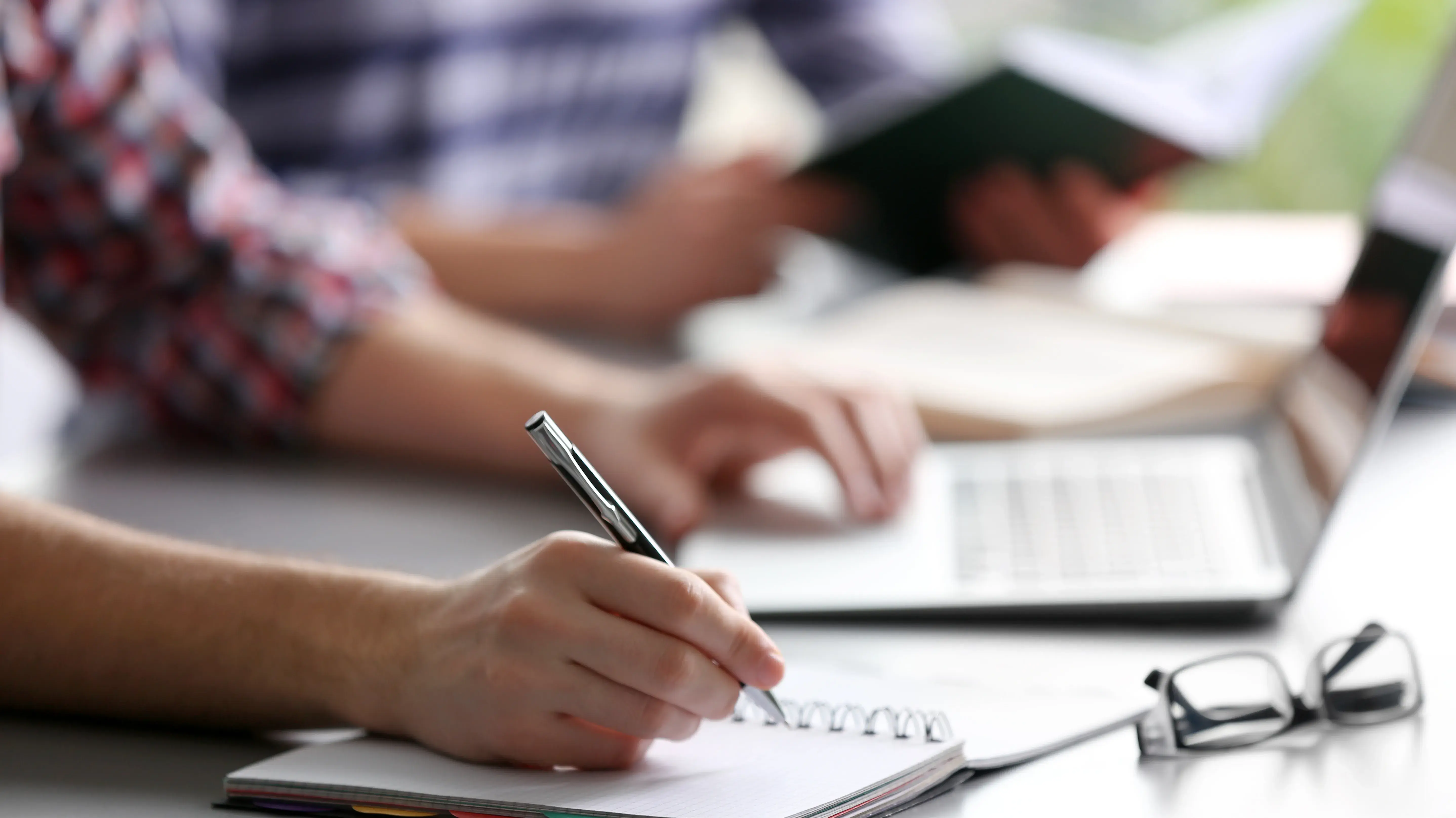 Student's hand writing in exercise book at the table