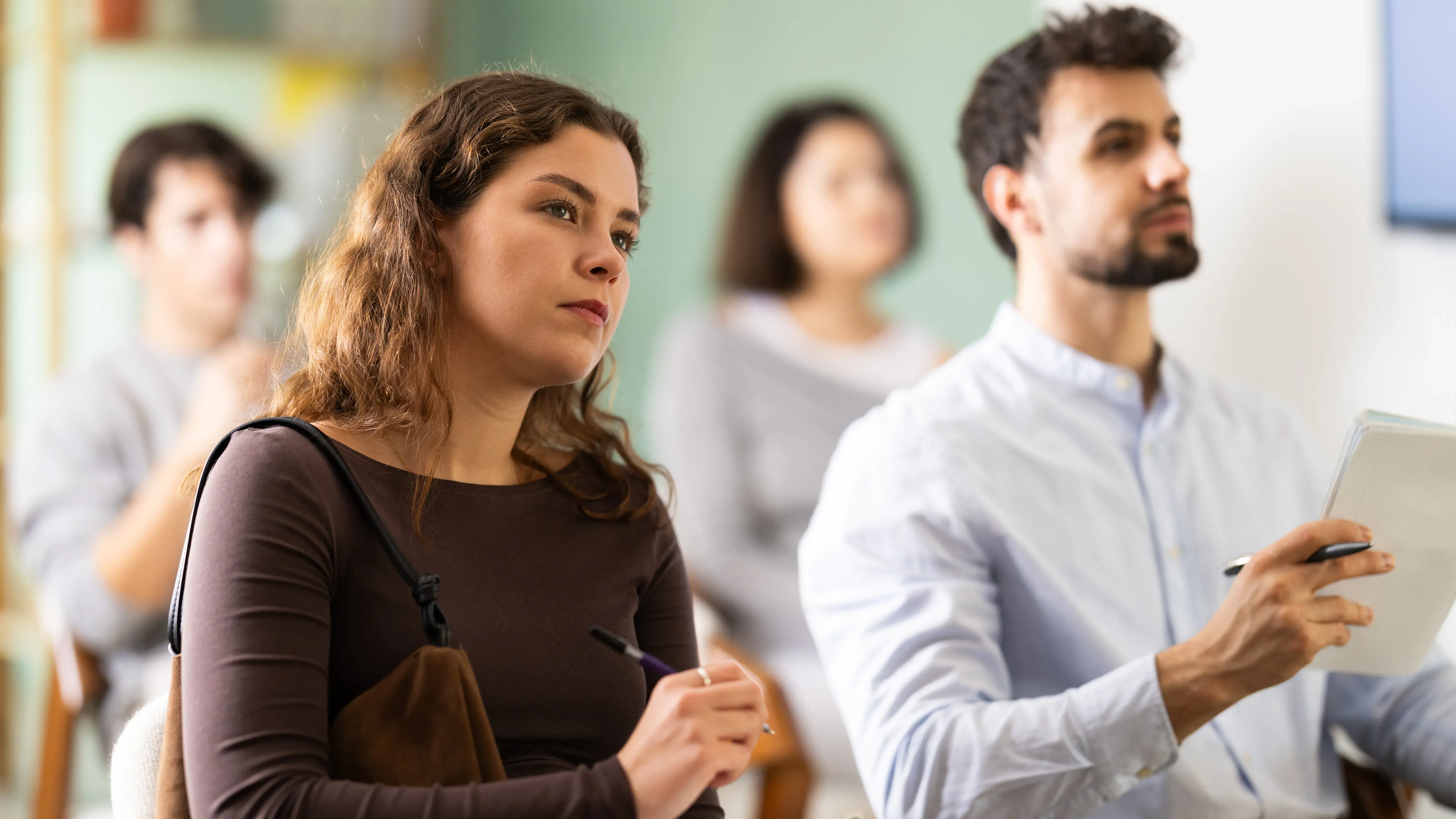 Woman listens attentively to teacher and takes notes in notebook during a professional development course
