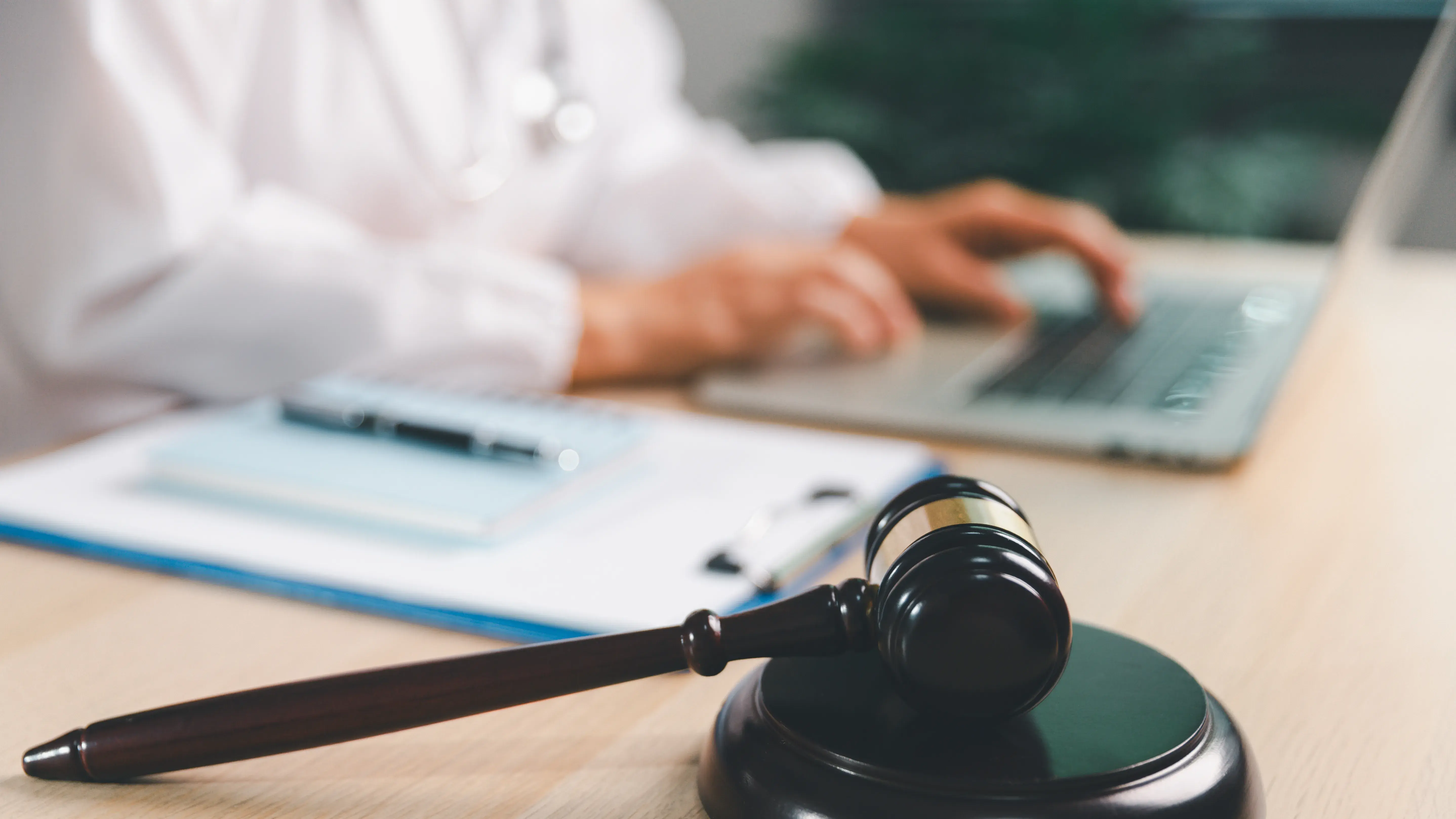 Healthcare law concept with gavel in focus as medical professional uses laptop at office desk, representing digital compliance, malpractice, liability, ethics and legal research