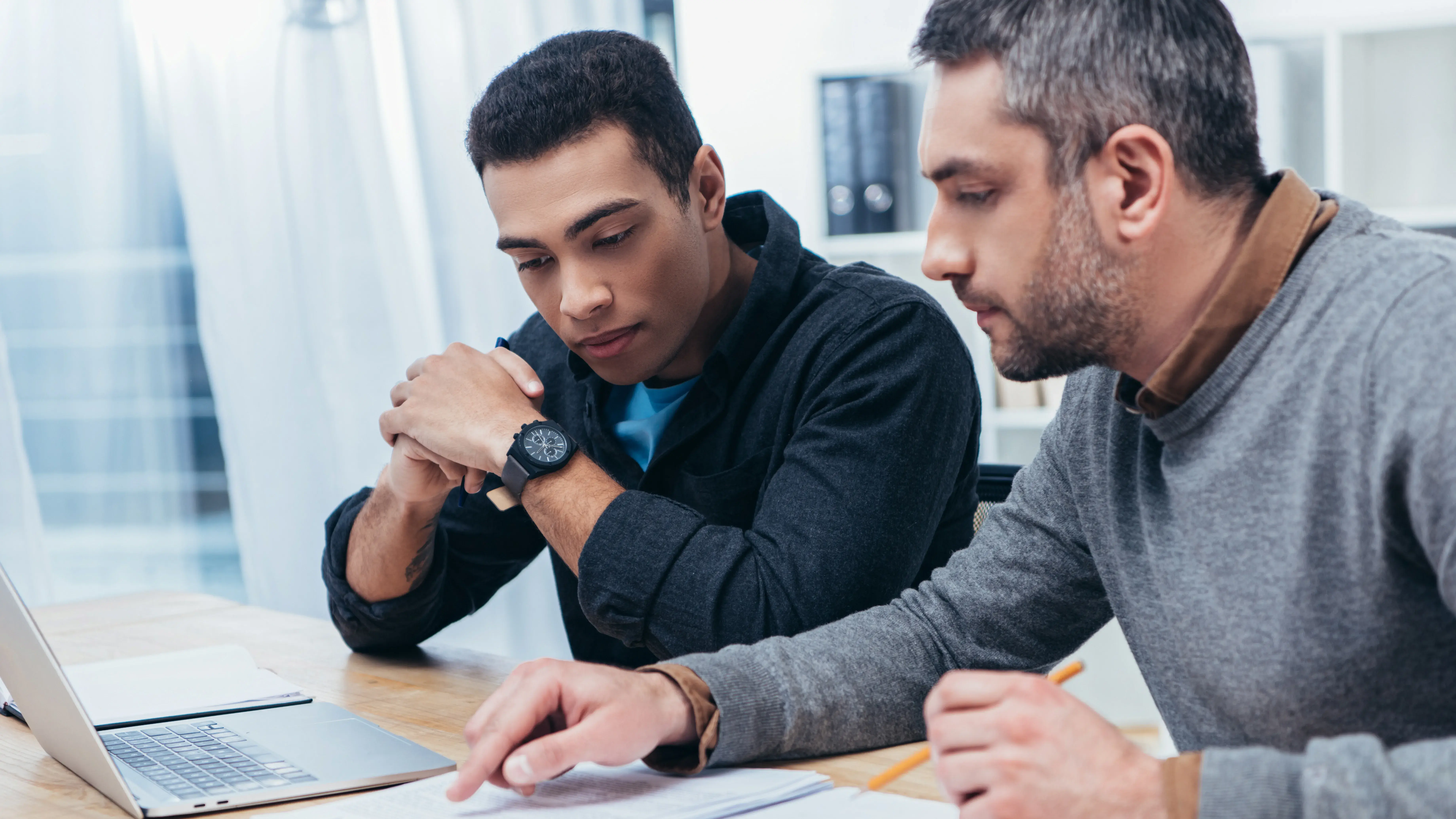 two males reading a piece of paper on a table, one of them seems to be lecturing the other